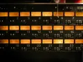 Panneau d'équipement audio avec 24 indicateurs VU orange, chacun affichant un niveau sonore, certains proches de 0 dB, équivalent à 64 décibels.