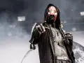Un membre d'un groupe metal masqué, le visage peint de rouge et blanc, pointe du doigt.
