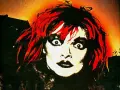 Visage intense d'une femme aux cheveux rouges et maquillage prononcé, évoquant l'esthétique d'un groupe allemand des années 90.