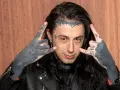 Un membre de Falling In Reverse, avec des tatouages sur le visage et les mains, fait le signe des cornes.