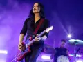 Brian Molko, le chanteur de Placebo, joue de la guitare rouge sur scène, éclairé par des lumières violettes.
