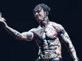 Le chanteur de Falling In Reverse, Ronnie Radke, torse nu et couvert de tatouages colorés, lève le majeur sur scène.