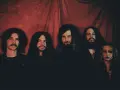 Cinq membres du groupe Uncle Acid and the Deadbeats posent devant un rideau rouge.