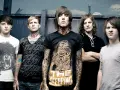 Cinq membres du groupe Bring Me The Horizon posent devant une clôture. Le chanteur porte un t-shirt avec un tigre et le texte "The Sleeping".