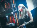 Une dj femme, casquette blanche et casque sur les oreilles, mixe dans une ambiance lumineuse et électrique.
