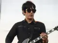Un des membres de Eagles of Death Metal, guitariste en chemise noire et lunettes de soleil, joue sur scène.