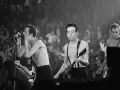 Le chanteur de The Clash, Joe Strummer, chante avec passion devant une foule en délire, guitare à la main.