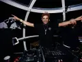 Un dj rap souriant, casqué, bras écartés, anime la soirée dans une cabine panoramique.