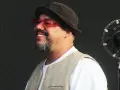 Un chanteur soul souriant, portant un chapeau et des lunettes rouges, se tient devant un microphone.