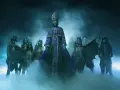 Les membres de Ghost (groupe) apparaissent dans une brume bleutée, le leader en robe violette imposante, entouré de squelettes masqués et d'une silhouette à chapeau.