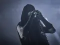 Chanteur de Dimmu Borgir, visage encapuchonné et maquillé, chantant dans un micro, ambiance sombre et enfumée.