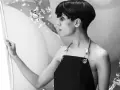 Fatima Al Qadiri, artiste à la coupe courte, porte un tablier noir, regardant une œuvre abstraite.