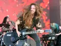 Reba Meyers, guitariste au look sauvage, fait vibrer sa guitare électrique sur scène, cheveux au vent, devant un fond rougeoyant.