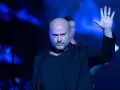 Le chanteur Disturbed, chauve et barbu, lève la main sur scène sous des lumières bleues intenses.