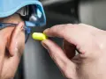 Main tenant, casque bleu, lunettes de protection et bouchon d'oreille jaune pour se protéger d'un bruit de 120 décibels équivalent.