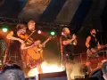 Un groupe celtique français sur scène, avec violon, guitare et basse. Les musiciens portent des kilts, créant une ambiance festive.