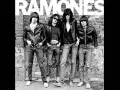 Les Ramones, quatre icônes punk en blousons de cuir et jeans, posent devant un mur de briques tagué.