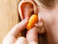 Une main insère une boule quies orange dans une oreille pour réduire les décibels.