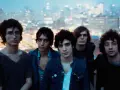 Les membres de The Strokes posent ensemble, le regard tourné vers l'objectif, avec une ville illuminée en arrière-plan.