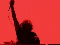 Chanteur de Rage Against the Machine, micro levé, sur fond rouge vif. L'énergie de leurs albums en live.