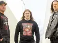 Trois hommes posent devant un mur. L'un porte un t-shirt avec une image de fœtus mourant.