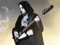 Le bassiste d'un groupe metal connu, maquillé et tatoué, joue sur scène, drapé dans une cape noire.