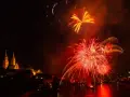 Feu d'artifice rougeoyant illuminant le ciel nocturne au-dessus d'une ville et d'une rivière. Le **décibel feu d'artifice** résonne dans l'air.