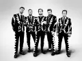 Les membres de The Hives posent en costumes noirs et blancs à motifs d'éclairs et de notes de musique.