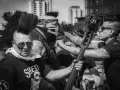 Quatre musiciens au look punk, dont un avec un bandana et un masque de crâne, se préparent à jouer. Un d'eux tient une contrebasse, prêt à faire un mad sin.
