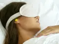 Femme dormant avec un masque et des boules quies pour éviter le bruit, utile en cas d'otite ou pour un sommeil paisible.