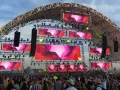 Scène de festival avec écrans LED diffusant des visuels abstraits roses et violets. Une foule danse sous la structure, attendant leur artiste deep house préféré.