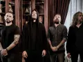 Quatre musiciens, dont un avec une capuche, posent devant des étagères remplies de livres. Ce groupe metal français connu dégage une aura mystérieuse.
