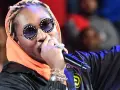 Un rappeur à la mode, avec des lunettes stylées et de nombreux bijoux, chante sur scène.