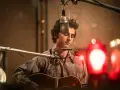 Un jeune homme à la guitare et à l'harmonica, dans un style de musique rappelant Bob Dylan, enregistre en studio.