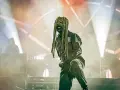 Un membre de Slipknot, masqué et en combinaison, sur scène sous des projecteurs.