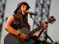 Une artiste de Hiatus Kaiyote, casquette sur la tête, chante et joue de sa guitare bleue étincelante sur scène.