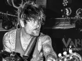 Un guitariste tatoué, cheveux en bataille, sous les projecteurs du VART. Kobe Liveact Bar.