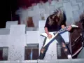 Guitariste aux cheveux longs, en plein solo, tel un maître des marionnettes sur scène.