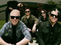 Les membres de The Offspring posent ensemble, souriants et portant des lunettes de soleil. Le groupe semble prêt pour une nouvelle aventure musicale.