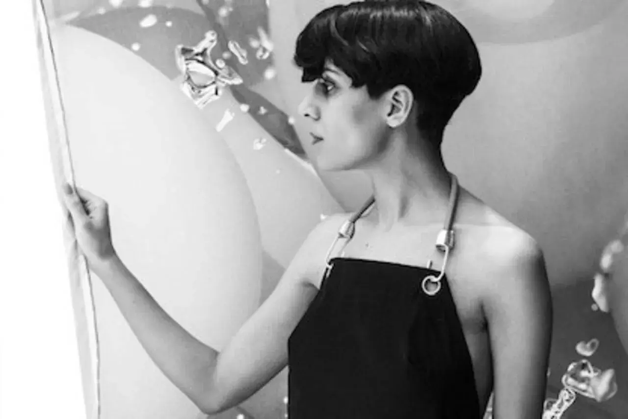 Fatima Al Qadiri, artiste à la coupe courte, porte un tablier noir, regardant une œuvre abstraite.