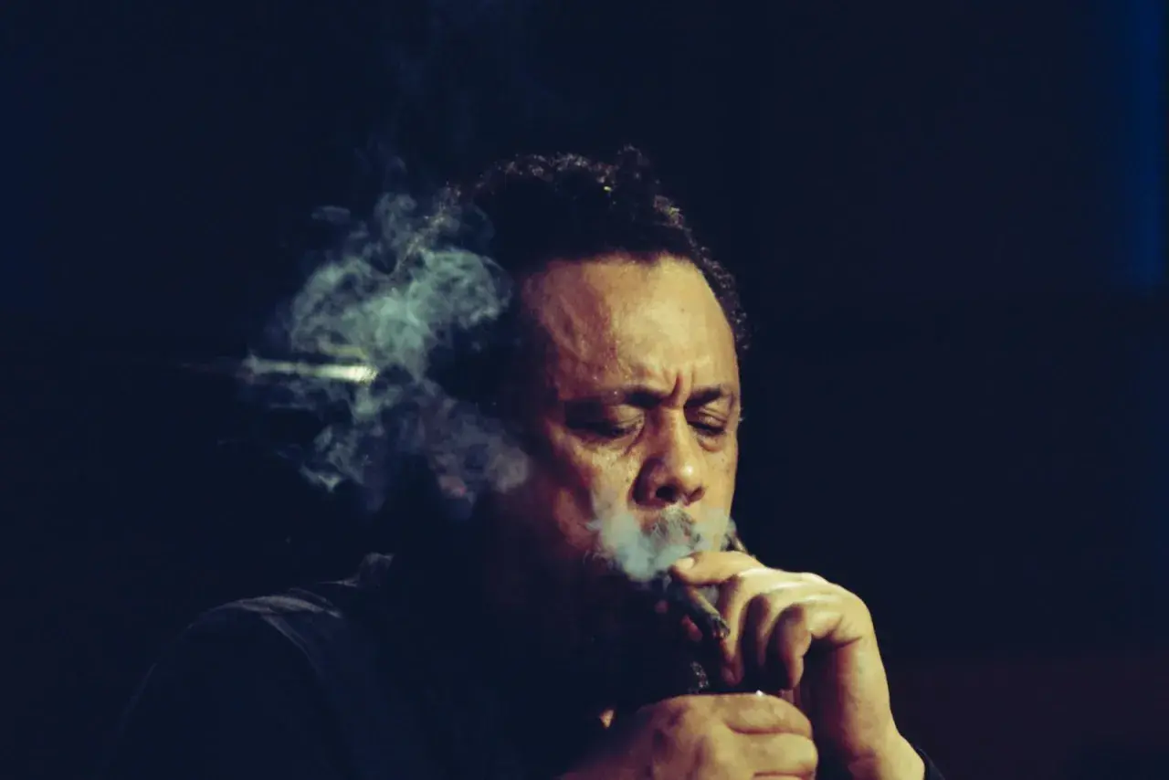 Charlie Mingus, le légendaire contrebassiste, exhale une fumée épaisse, les yeux clos, absorbé par sa musique.