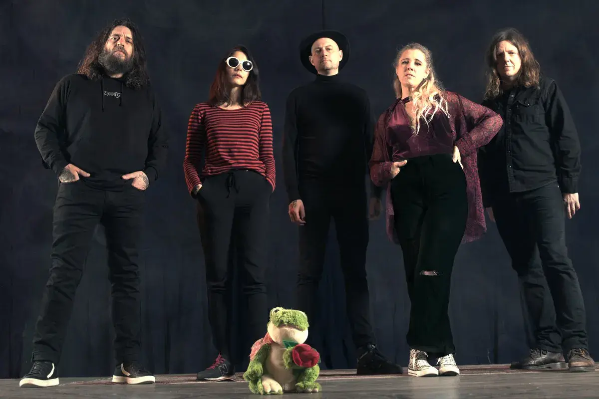 Cinq personnes se tiennent devant un fond sombre. Au premier plan, une grenouille en peluche tient une rose. Le groupe, comme un **crippled black phoenix**, semble prêt à s'envoler.