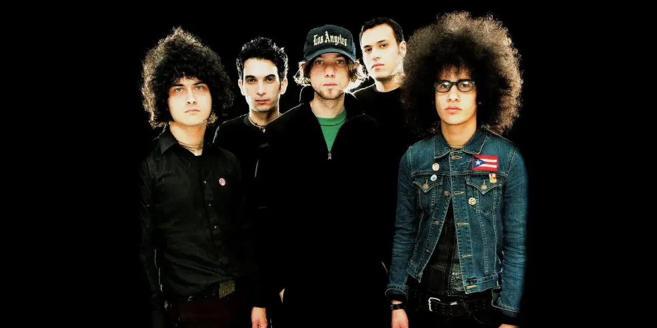 Cinq musiciens, dont certains avec des coiffures afro, posent pour une photo de groupe. L'un porte une casquette "Los Angeles". Ils sont prêts pour une soirée **at the drive in**.