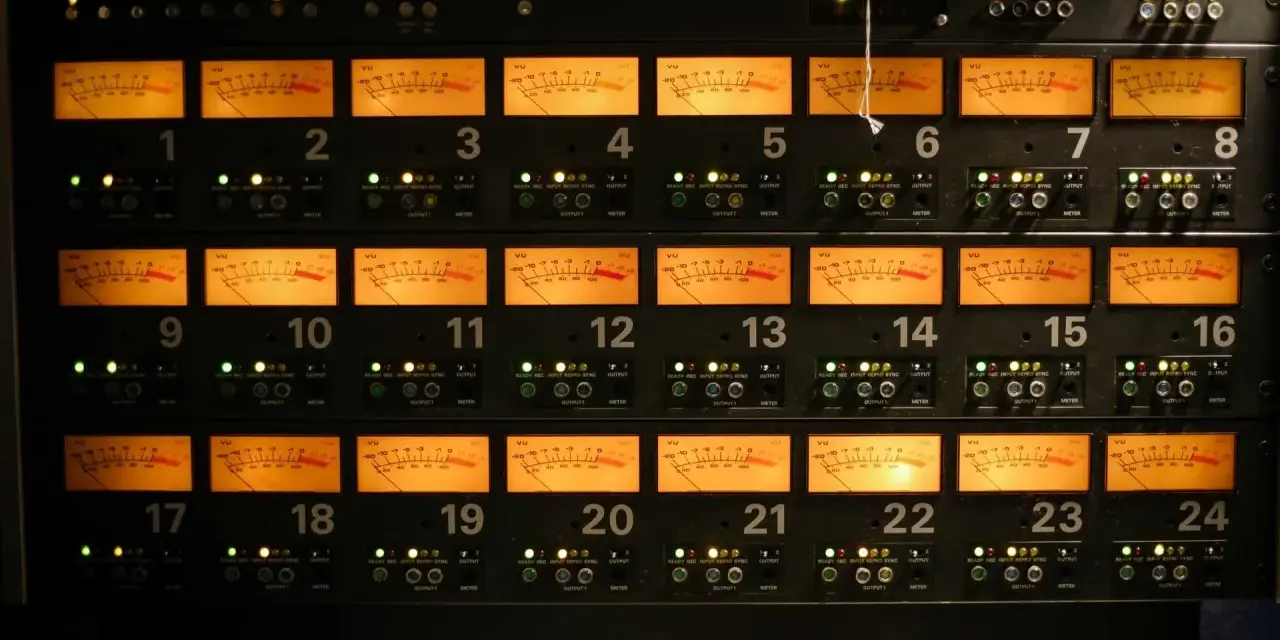 Panneau d'équipement audio avec 24 indicateurs VU orange, chacun affichant un niveau sonore, certains proches de 0 dB, équivalent à 64 décibels.
