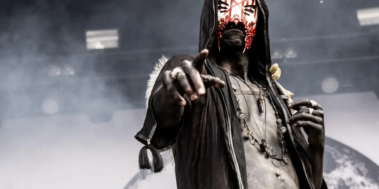 Un membre d'un groupe metal masqué, le visage peint de rouge et blanc, pointe du doigt.