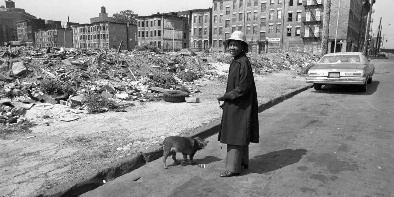 Une femme et son chien devant des immeubles délabrés et des décombres.