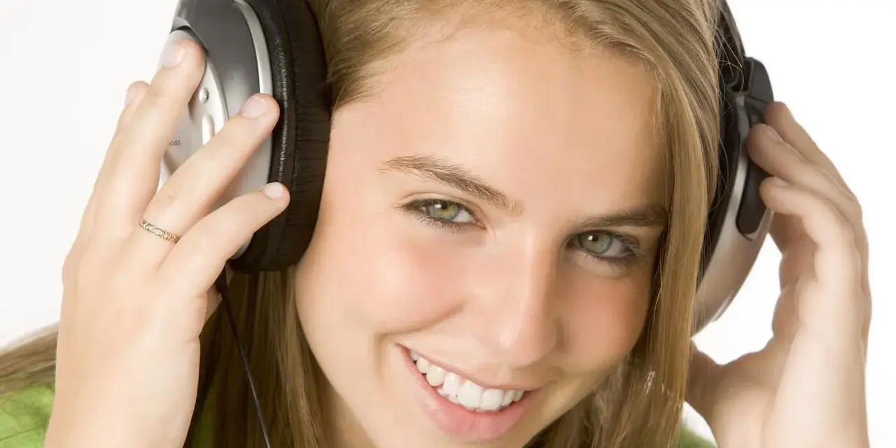 Jeune femme souriante avec des écouteurs, profitant de sa musique à 110 décibels.