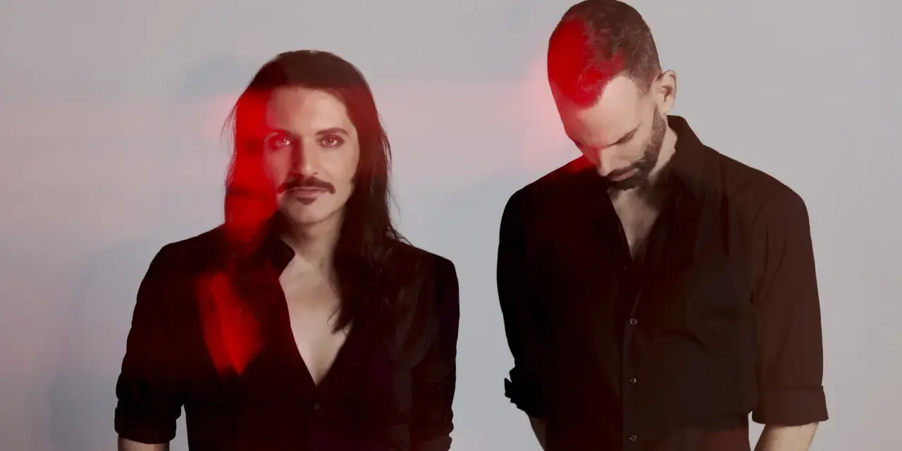 Les membres de Placebo, Brian Molko et Stefan Olsdal, posent en noir et blanc avec des éclats de lumière rouge.