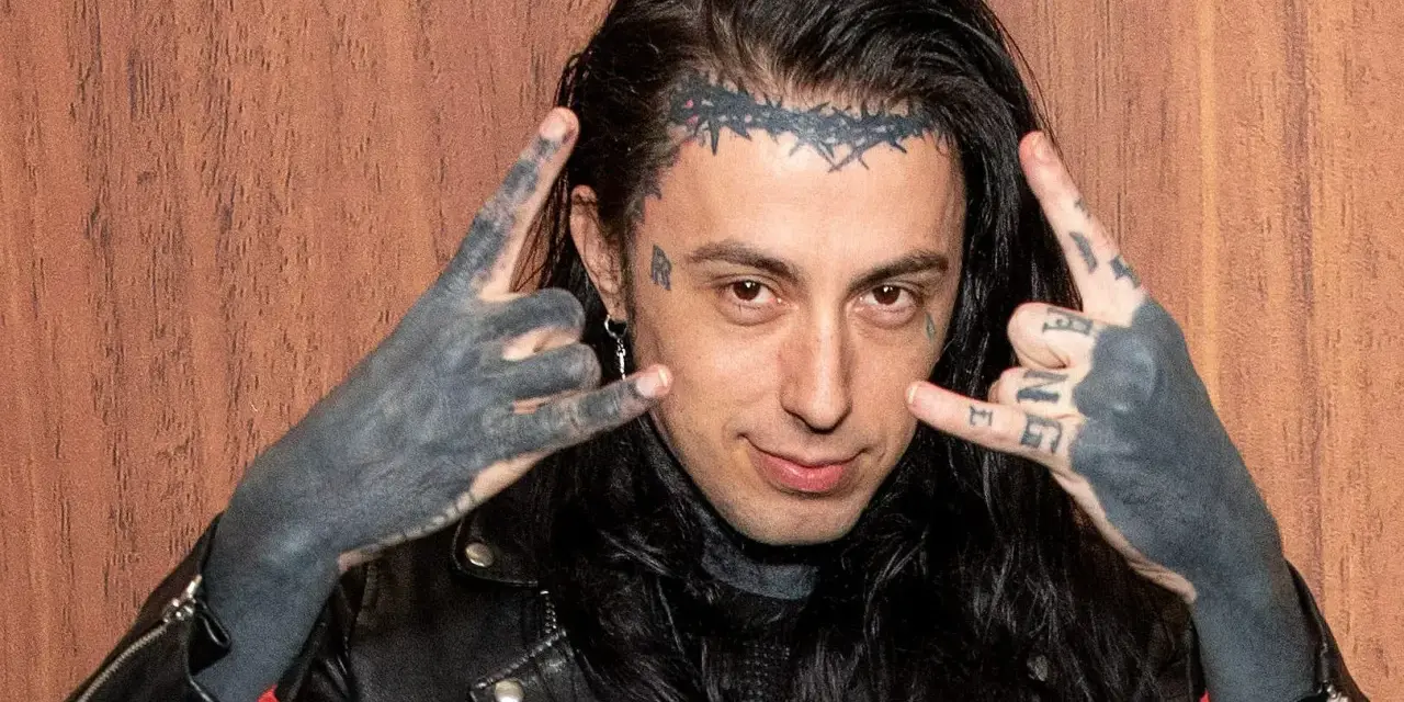 Un membre de Falling In Reverse, avec des tatouages sur le visage et les mains, fait le signe des cornes.