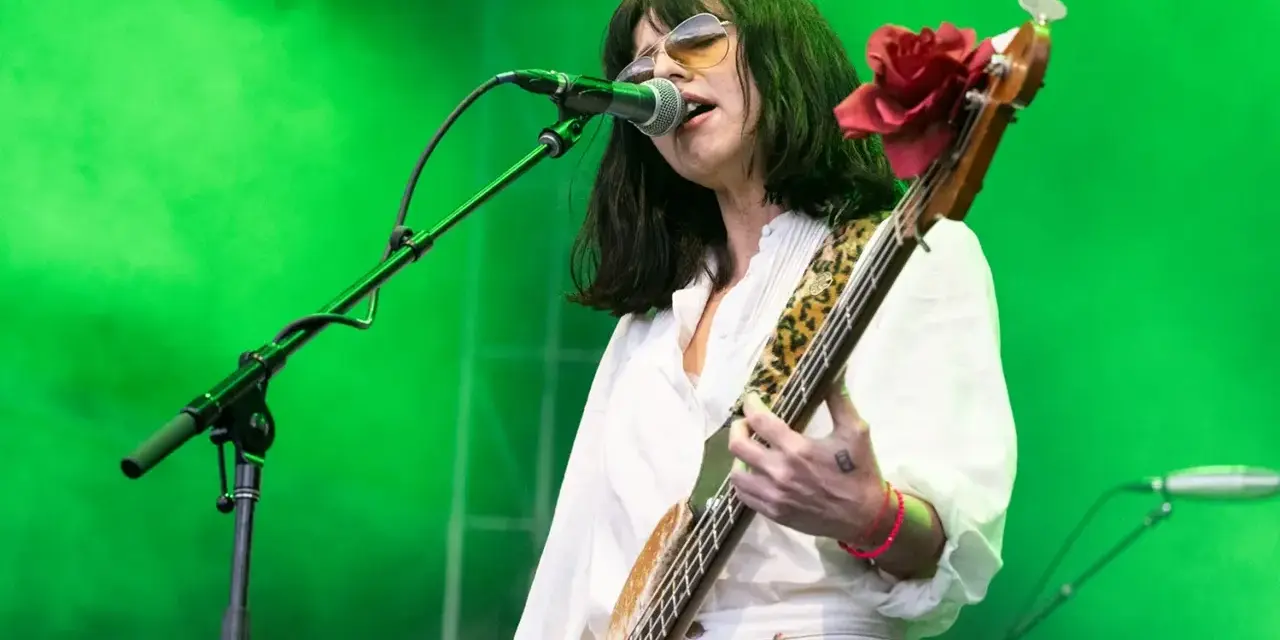 La chanteuse des Pixies, Kim Deal, joue de la basse sur scène, éclairée par une lumière verte.